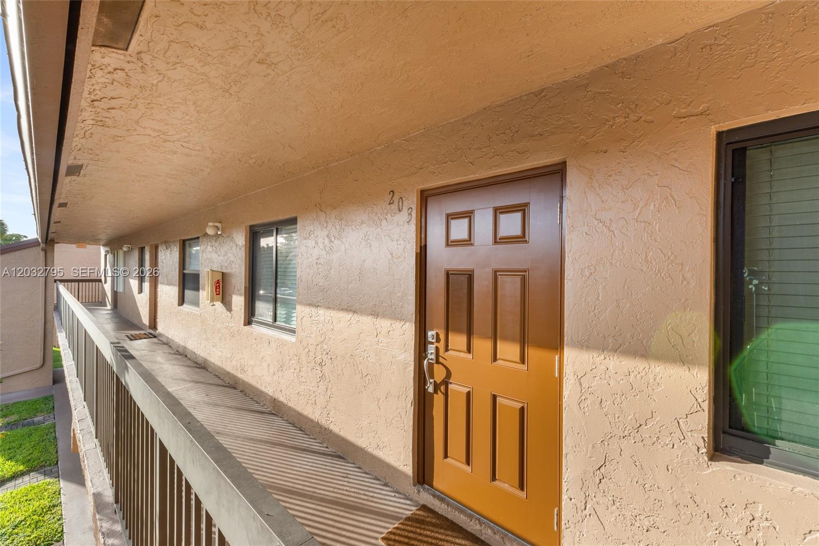 An exterior walkway leads to a brown door labeled 203 in a stucco building — 10003 Winding Lake Rd # 203, Sunrise FL 33351, SUNRISE, FL