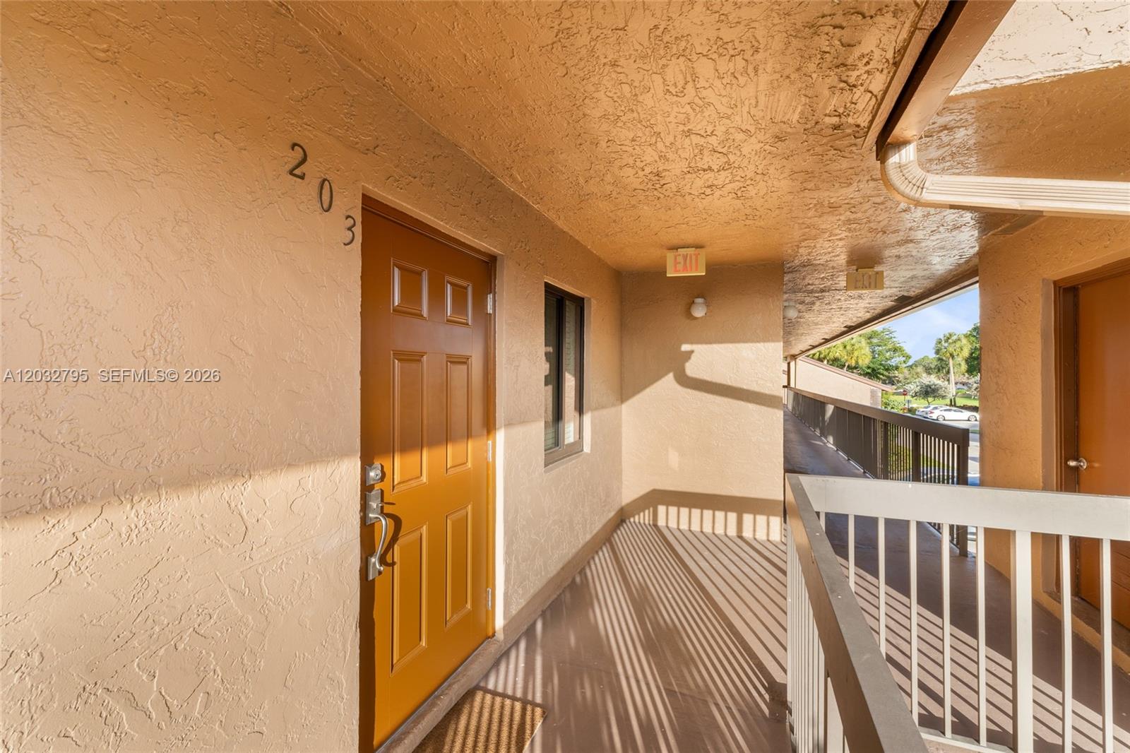 An exterior apartment hallway features a brown door labeled 203 and a white metal railing — 10003 Winding Lake Rd # 203, Sunrise FL 33351, SUNRISE, FL