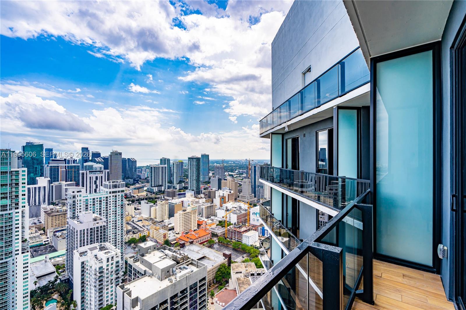 A high-rise balcony with glass railings overlooks a dense urban cityscape under a blue sky — 398 NE 5th St # 4716, Miami FL 33132, MIAMI, FL