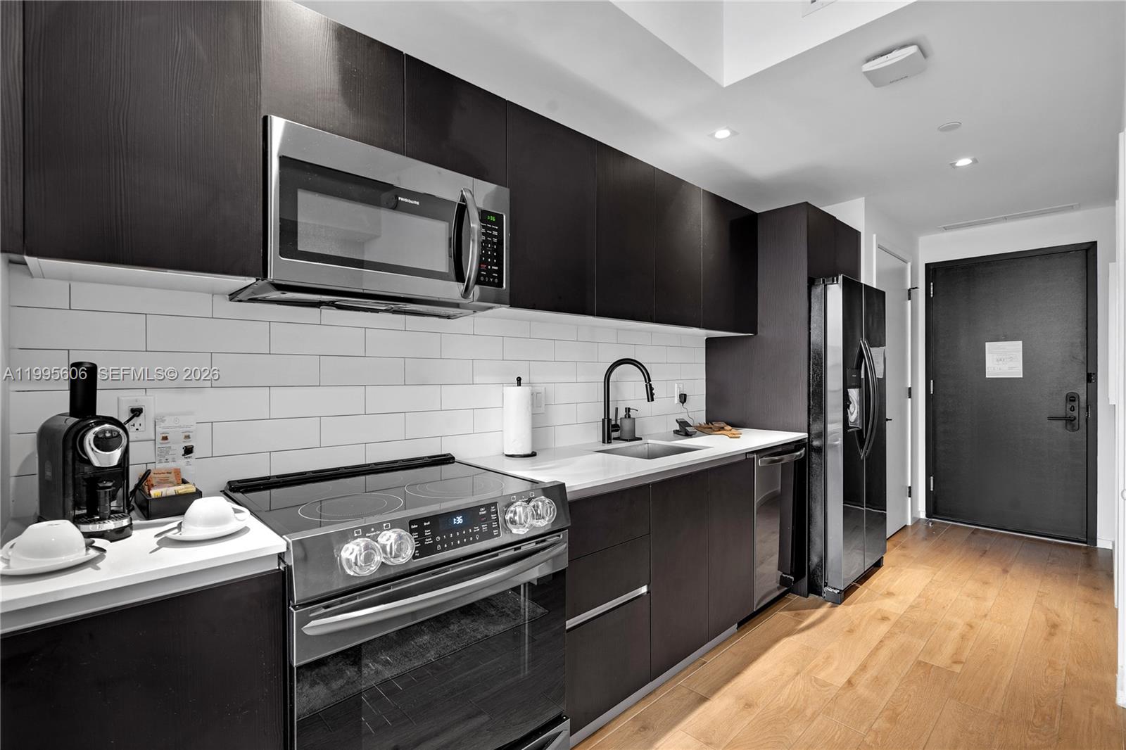 A modern kitchen features dark cabinetry, stainless steel appliances, white subway tile, and wood flooring — 398 NE 5th St # 4716, Miami FL 33132, MIAMI, FL