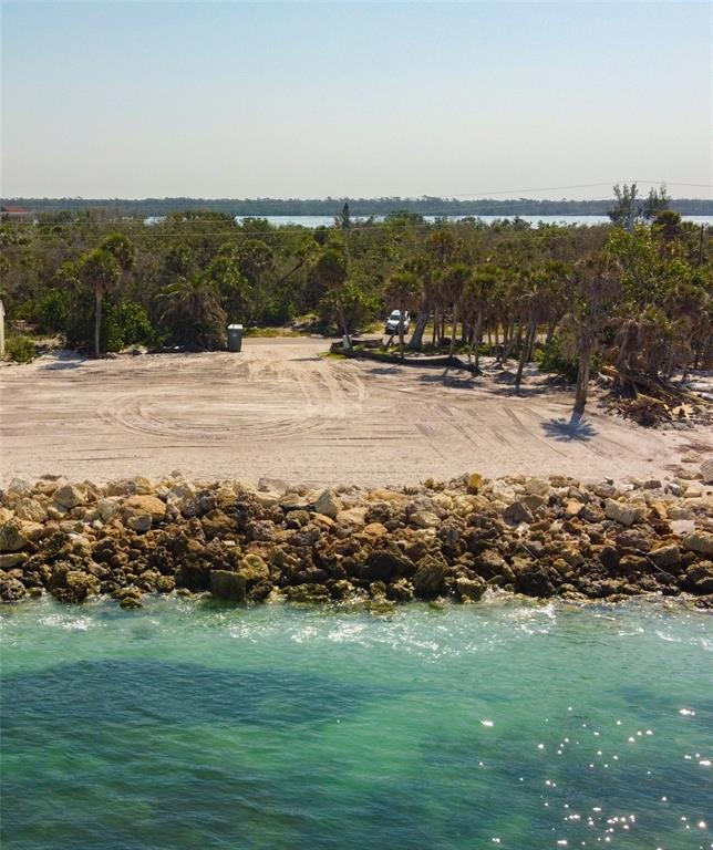 An aerial view of a vacant, sandy waterfront lot bordered by a rocky seawall — 7050 MANASOTA KEY ROAD, ENGLEWOOD, FL