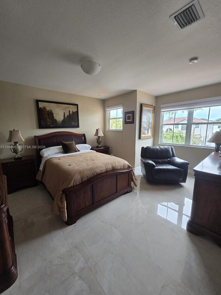 A bedroom features a wooden bed frame, tile flooring, a leather armchair, and two windows — 14978 SW 12th Ln # 0, Miami FL 33194, MIAMI, FL