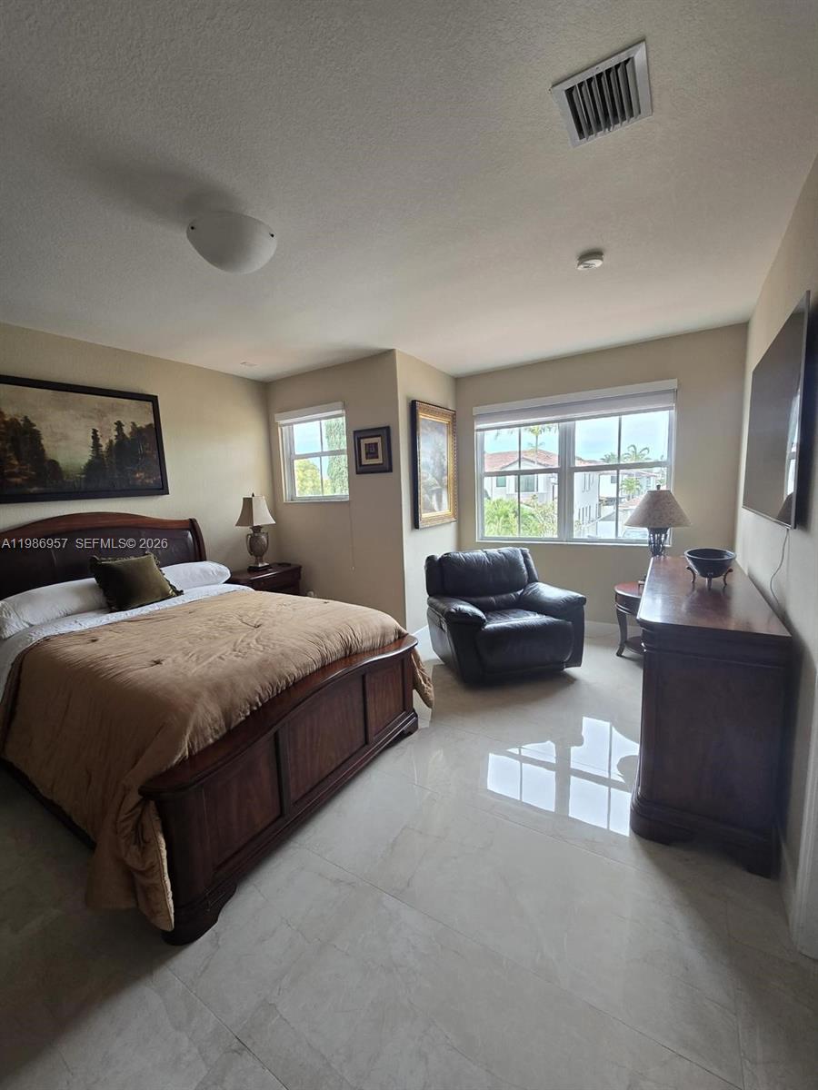 A bedroom features a wooden bed frame, a leather armchair, and light-colored tile flooring — 14978 SW 12th Ln # 0, Miami FL 33194, MIAMI, FL