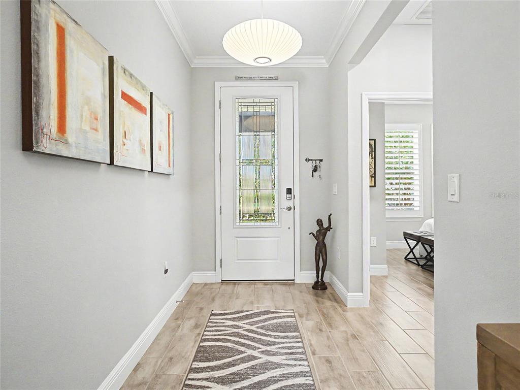 A bright entryway features light wood-look tile flooring, a white front door, and abstract wall art — 4235 NW 55TH COURT, OCALA, FL