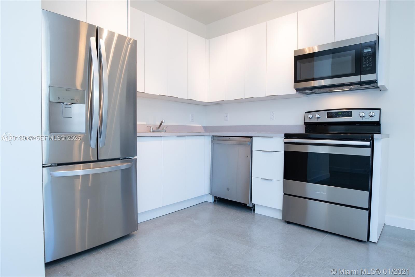A modern kitchen features white cabinets, stainless steel appliances, and gray tile flooring — 120 NE 71st St # 3, Miami FL 33138, MIAMI, FL