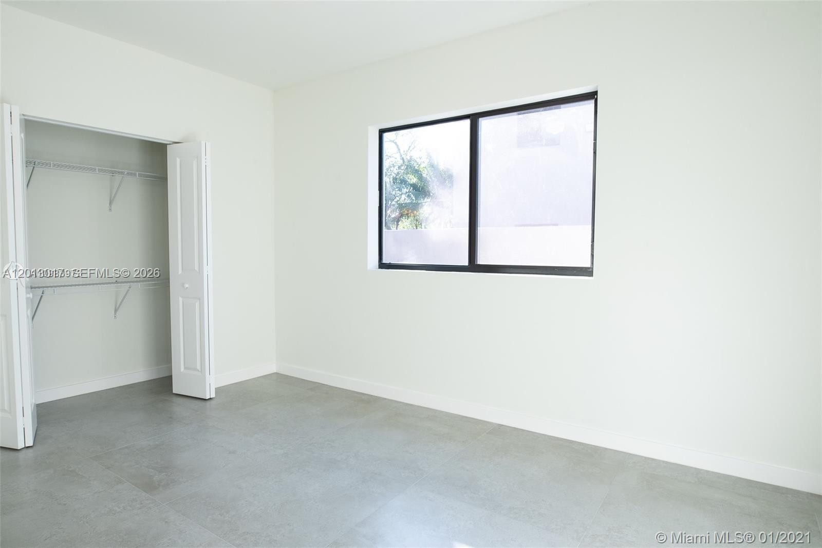 An empty bedroom features white walls, gray tile flooring, a window, and a walk-in closet — 120 NE 71st St # 3, Miami FL 33138, MIAMI, FL