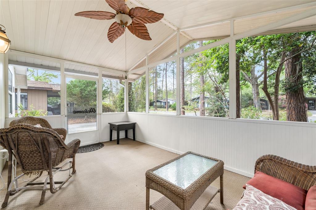 A screened-in porch features wicker furniture, a ceiling fan, and views of wooded surroundings — 8593 NW 41ST TERRACE, GAINESVILLE, FL