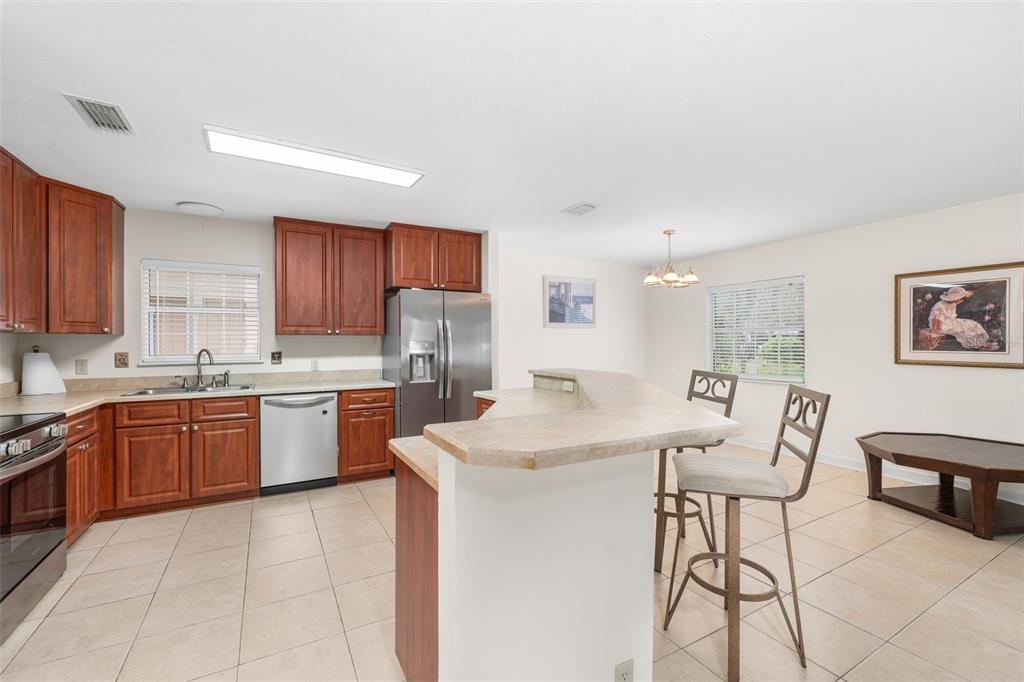 A kitchen features wood cabinets, stainless steel appliances, tile flooring, and a breakfast bar — 8593 NW 41ST TERRACE, GAINESVILLE, FL