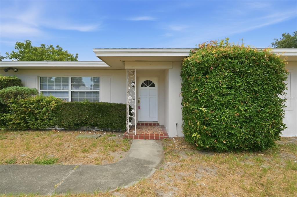 A single-story house exterior features a white front door, decorative metal column, and overgrown landscaping — 1981 TEMPLE TERRACE, CLEARWATER, FL