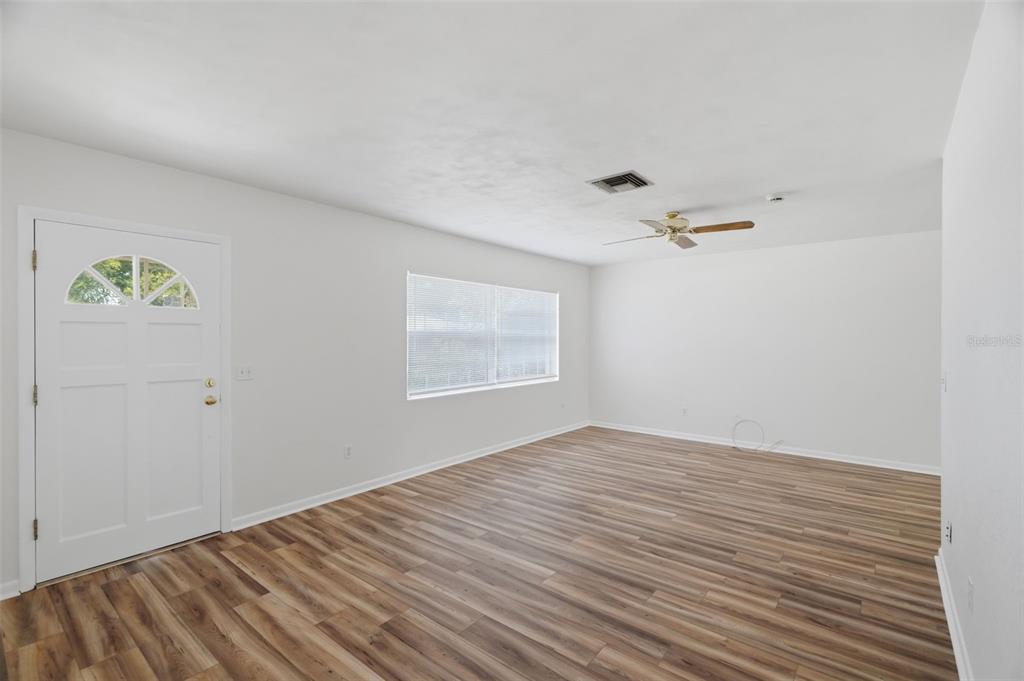 An empty living room features white walls, wood-look flooring, a ceiling fan, and a front door — 1981 TEMPLE TERRACE, CLEARWATER, FL