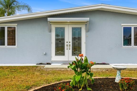 A light blue house exterior features a double glass front door and a small garden — 4127 GARDNER DRIVE, PORT CHARLOTTE, FL