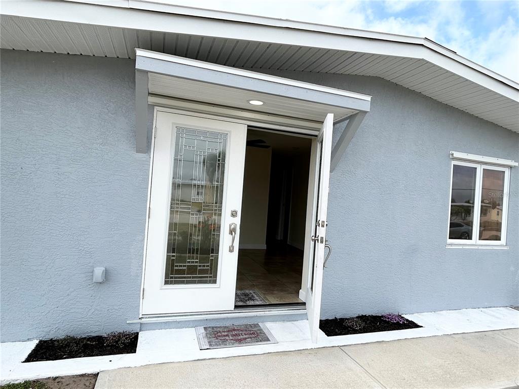 A light blue house exterior features a white front door with decorative glass panels — 4127 GARDNER DRIVE, PORT CHARLOTTE, FL