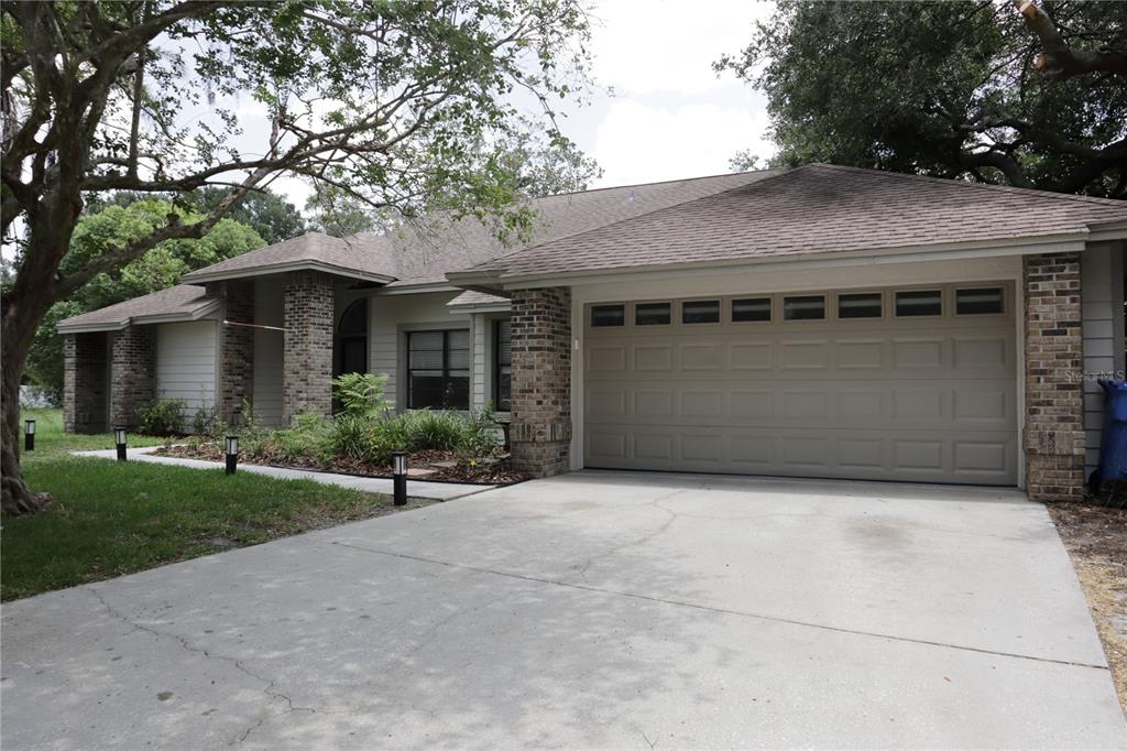 A single-story house with a beige garage door, brick accents, and a concrete driveway — 10428 TARA DRIVE, RIVERVIEW, FL