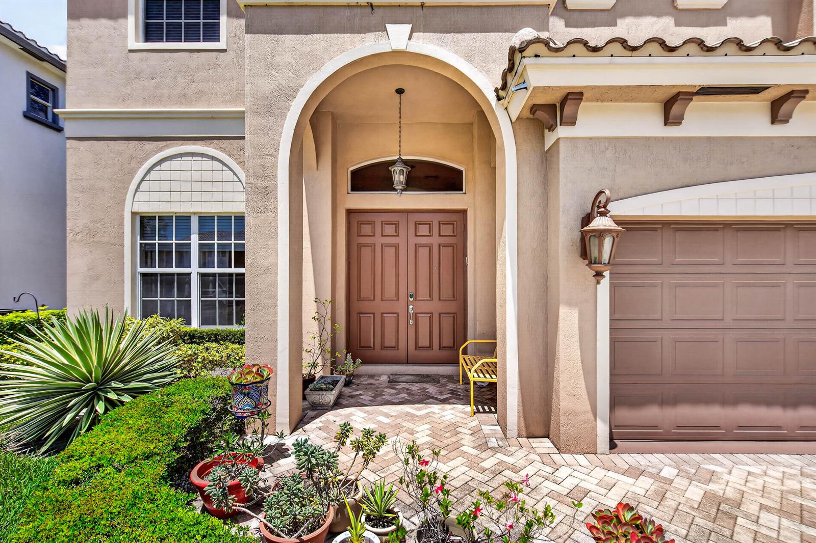A tan stucco house exterior features a brick-paved entryway, double front doors, and potted plants — 9898 Coronado Lake Drive, Boynton Beach FL 33437, BOYNTON BEACH, FL