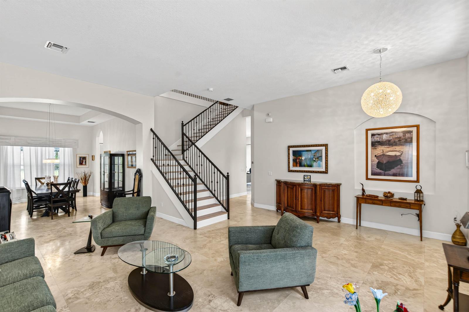 A living room with tile floors, a central staircase, and green armchairs facing a coffee table — 9898 Coronado Lake Drive, Boynton Beach FL 33437, BOYNTON BEACH, FL