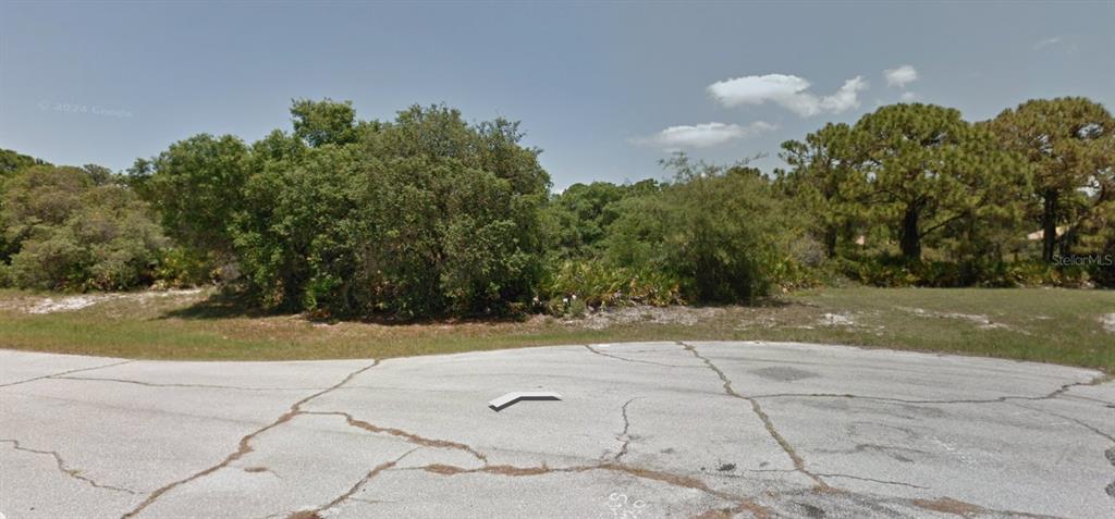 A vacant, wooded lot sits behind a cracked asphalt road under a clear blue sky — 103 WEST DRIVE, ROTONDA WEST, FL
