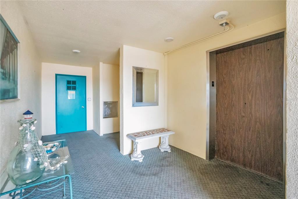 An interior hallway features a blue door, a wood-grain elevator door, and a small bench — 2960 59TH STREET S UNIT 405, GULFPORT, FL