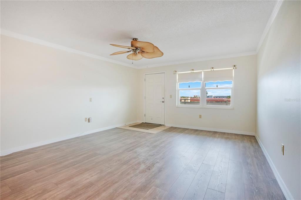 An empty room features light wood-look flooring, white walls, a ceiling fan, and a door — 2960 59TH STREET S UNIT 405, GULFPORT, FL