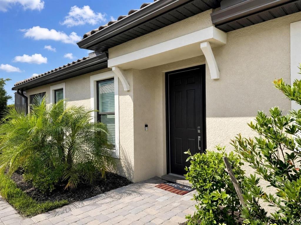 A beige stucco house exterior features a dark front door, white trim, and a paver walkway — 15514 VITTORIO STREET, NAPLES, FL