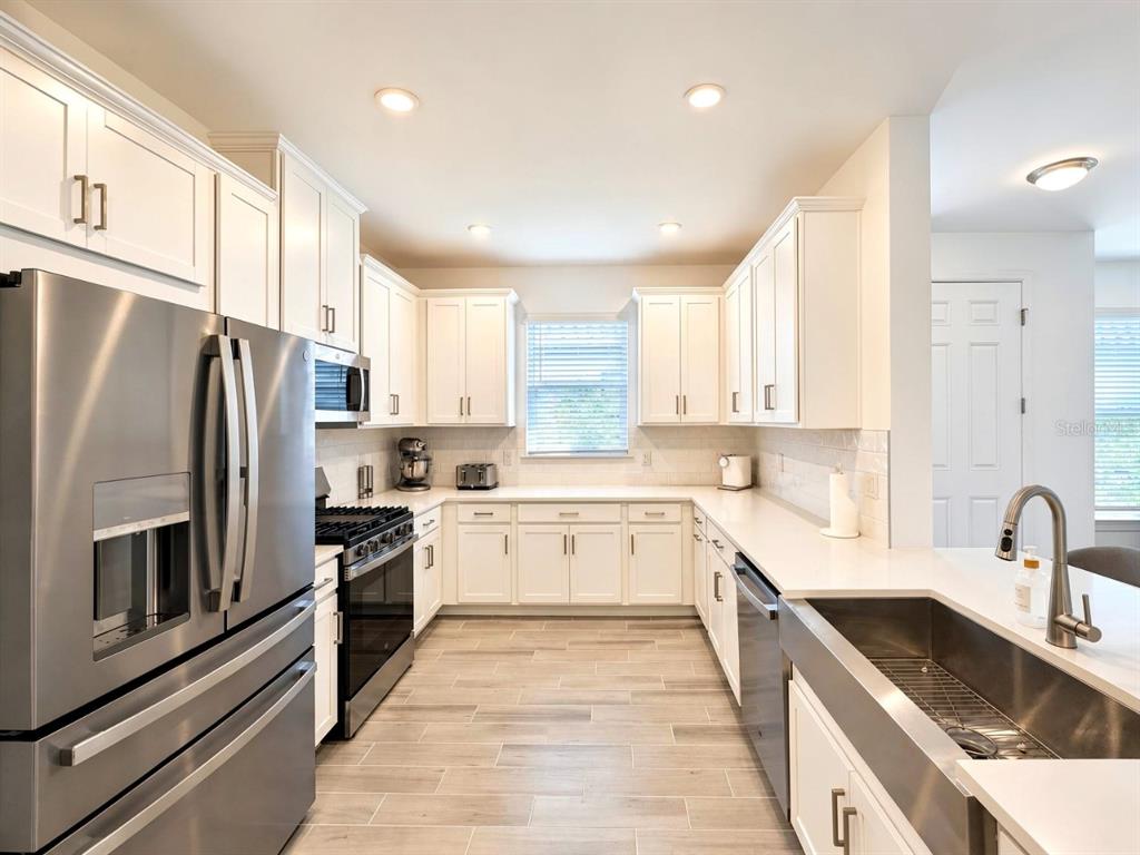 A modern kitchen features white cabinets, stainless steel appliances, and light wood-look tile flooring — 15514 VITTORIO STREET, NAPLES, FL