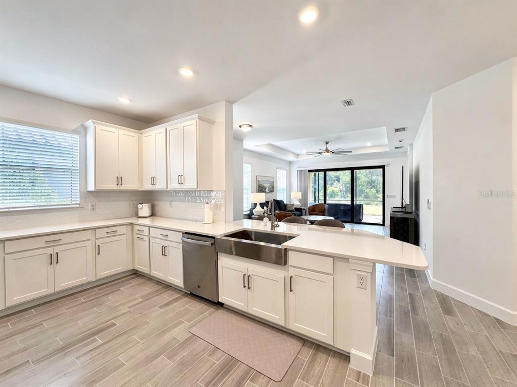A bright kitchen features white cabinets, a farmhouse sink, and light wood-look tile flooring — 15514 VITTORIO STREET, NAPLES, FL
