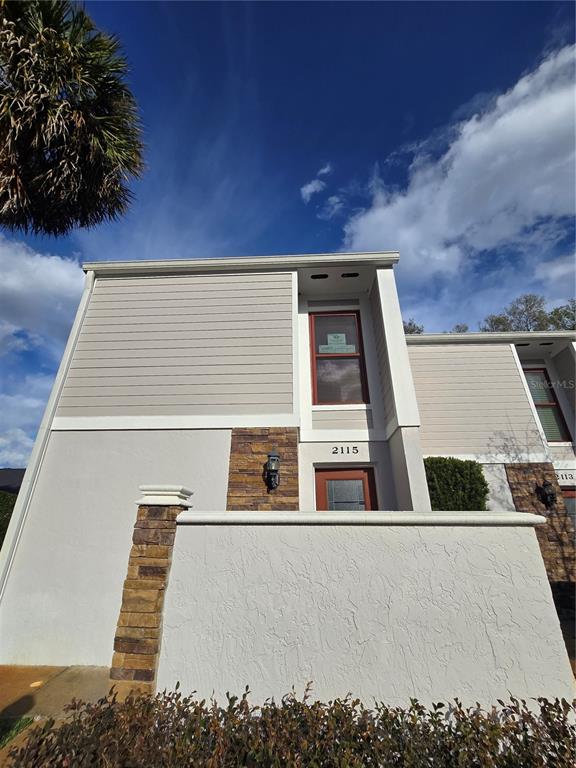A two-story townhouse exterior features beige siding, stone accents, and a white stucco wall — 2115 NE 38TH AVENUE, OCALA, FL