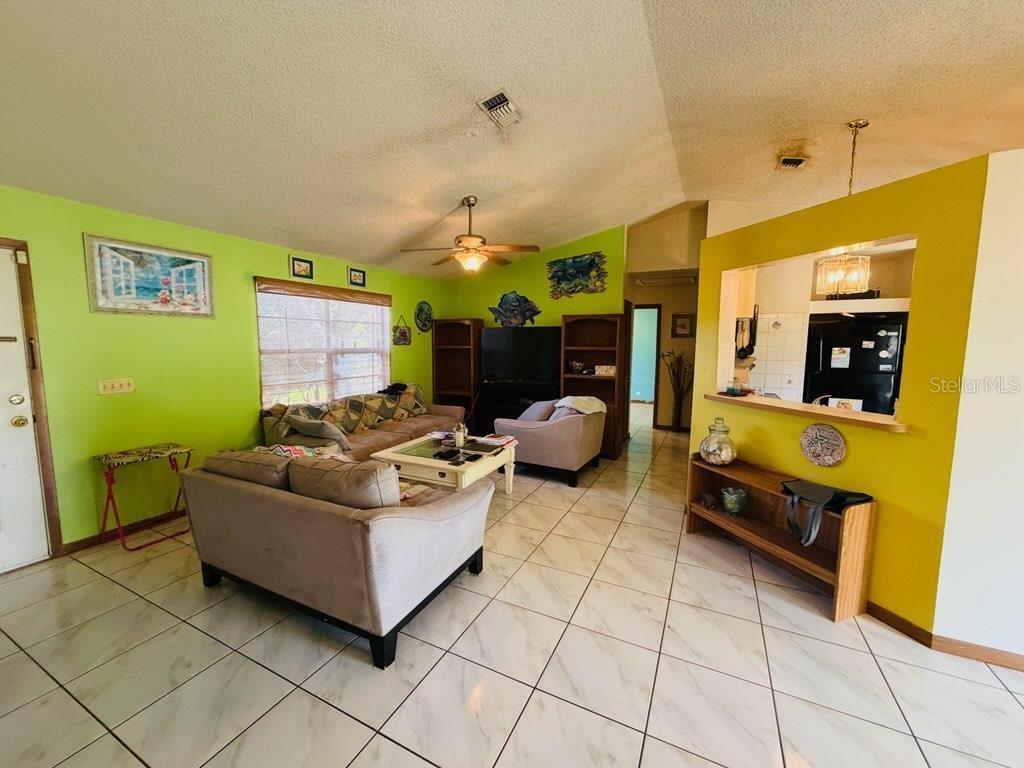 A living room with lime green walls, tile flooring, and an open pass-through to the kitchen — 450 TOPEKA, PALM BAY, FL