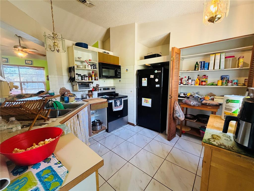 A kitchen features white tile flooring, a black refrigerator, a stove, and an open pantry — 450 TOPEKA, PALM BAY, FL