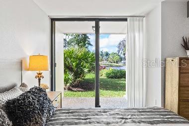 A bedroom features a bed, a bedside lamp, and a sliding glass door overlooking a lawn — 3071 WILLOW GREEN UNIT 35, SARASOTA, FL
