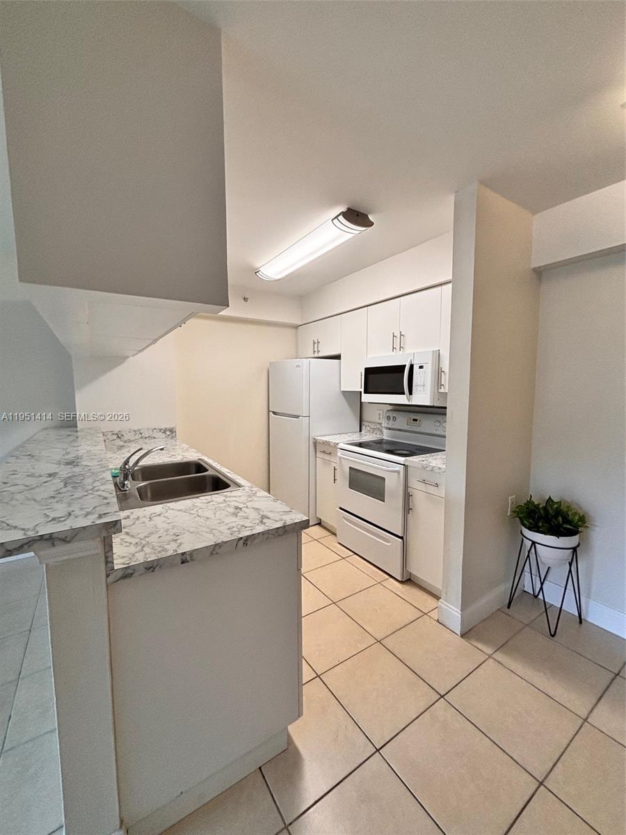 A kitchen features white cabinets, white appliances, and marble-patterned countertops over light-colored tile flooring — 450 S Park Rd # 104, Hollywood FL 33021, HOLLYWOOD, FL