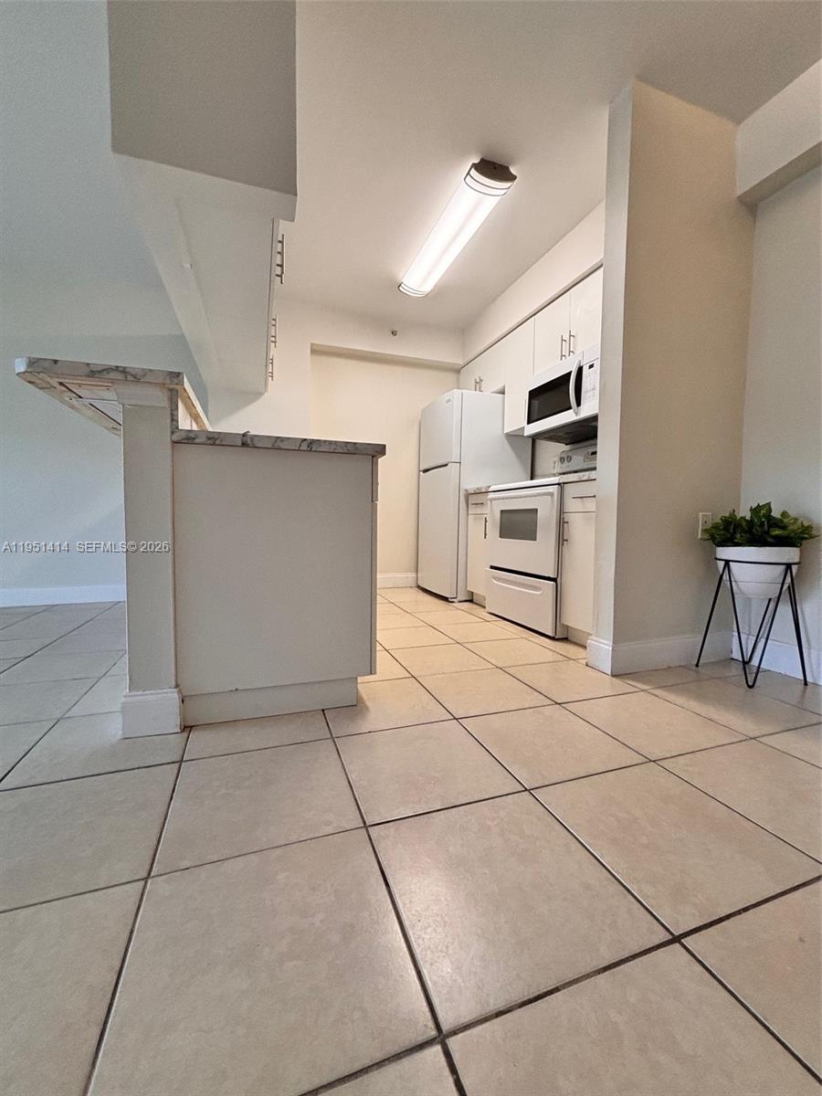 A kitchen features white cabinets, white appliances, and light-colored tile flooring — 450 S Park Rd # 104, Hollywood FL 33021, HOLLYWOOD, FL