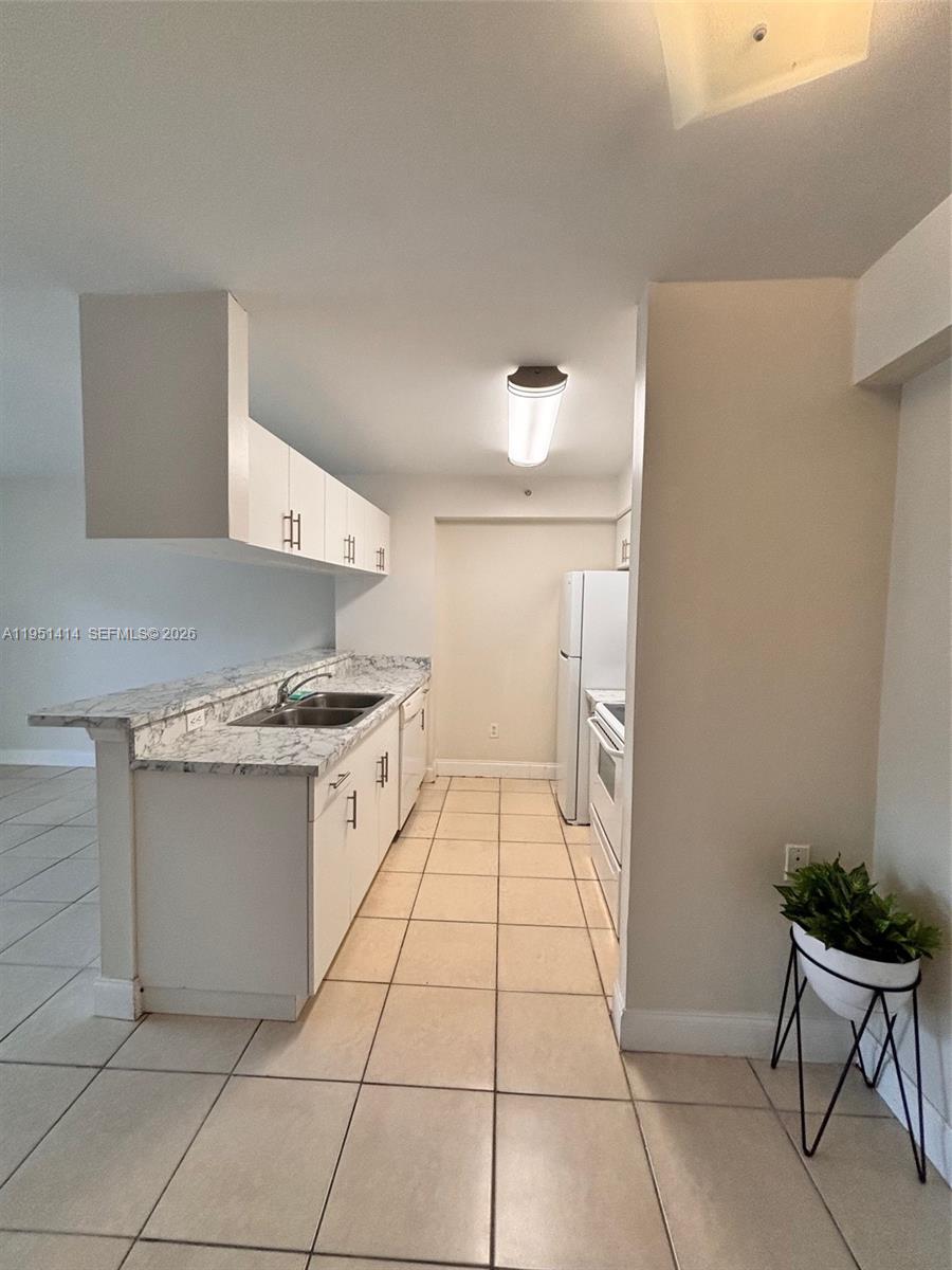 A galley-style kitchen features white cabinets, marble-patterned countertops, and light-colored floor tiles — 450 S Park Rd # 104, Hollywood FL 33021, HOLLYWOOD, FL