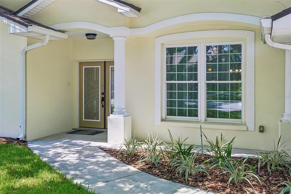 A beige house exterior features a covered entryway with a column and a large window — 818 VILLAGE WAY, PALM HARBOR, FL