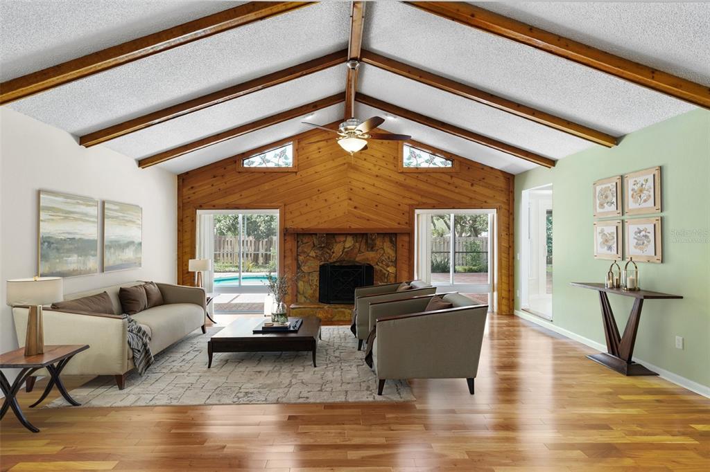 A living room features a vaulted ceiling with exposed beams, a stone fireplace, and hardwood floors — 818 VILLAGE WAY, PALM HARBOR, FL