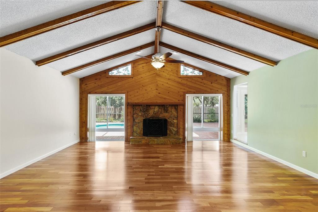 A spacious living room features a vaulted ceiling, wood paneling, a stone fireplace, and hardwood floors — 818 VILLAGE WAY, PALM HARBOR, FL