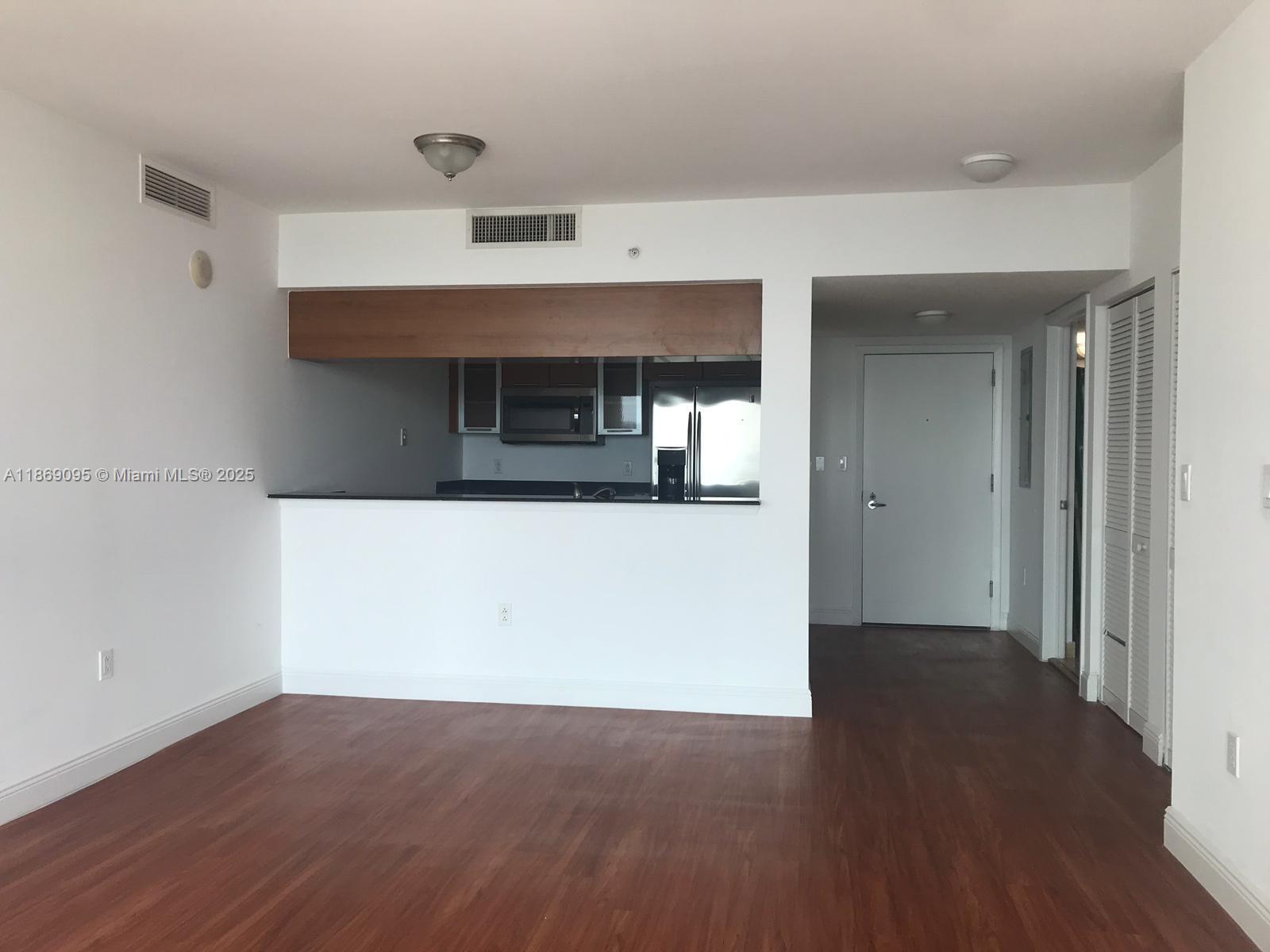 An interior view shows a living area with wood-look flooring, a kitchen pass-through, and an entryway — 1800 N Bayshore Dr # 3910, Miami FL 33132, MIAMI, FL