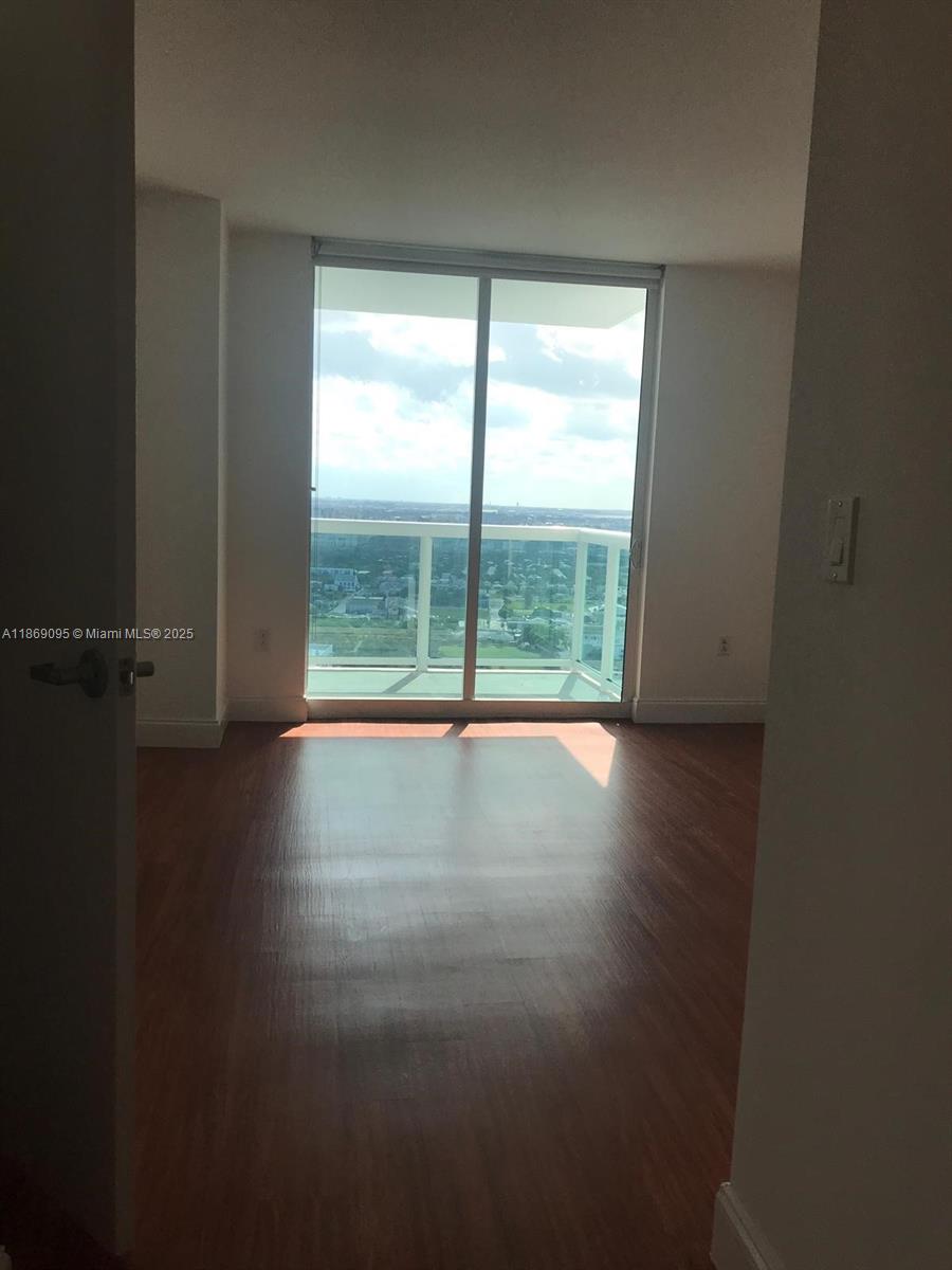 An empty room with wood-look flooring features a large sliding glass door leading to a balcony — 1800 N Bayshore Dr # 3910, Miami FL 33132, MIAMI, FL