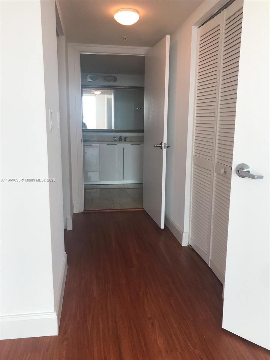 A hallway with wood-look flooring leads to a bathroom with white cabinets and a mirror — 1800 N Bayshore Dr # 3910, Miami FL 33132, MIAMI, FL