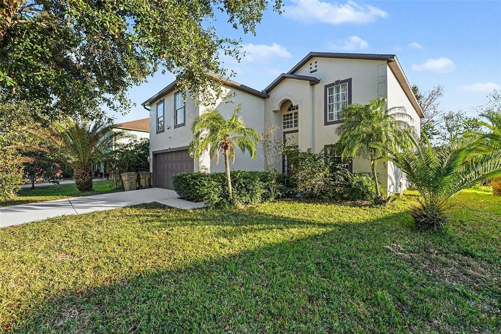A two-story suburban house with a beige stucco exterior, a garage, and palm trees — 2355 ANDREWS VALLEY DRIVE, KISSIMMEE, FL