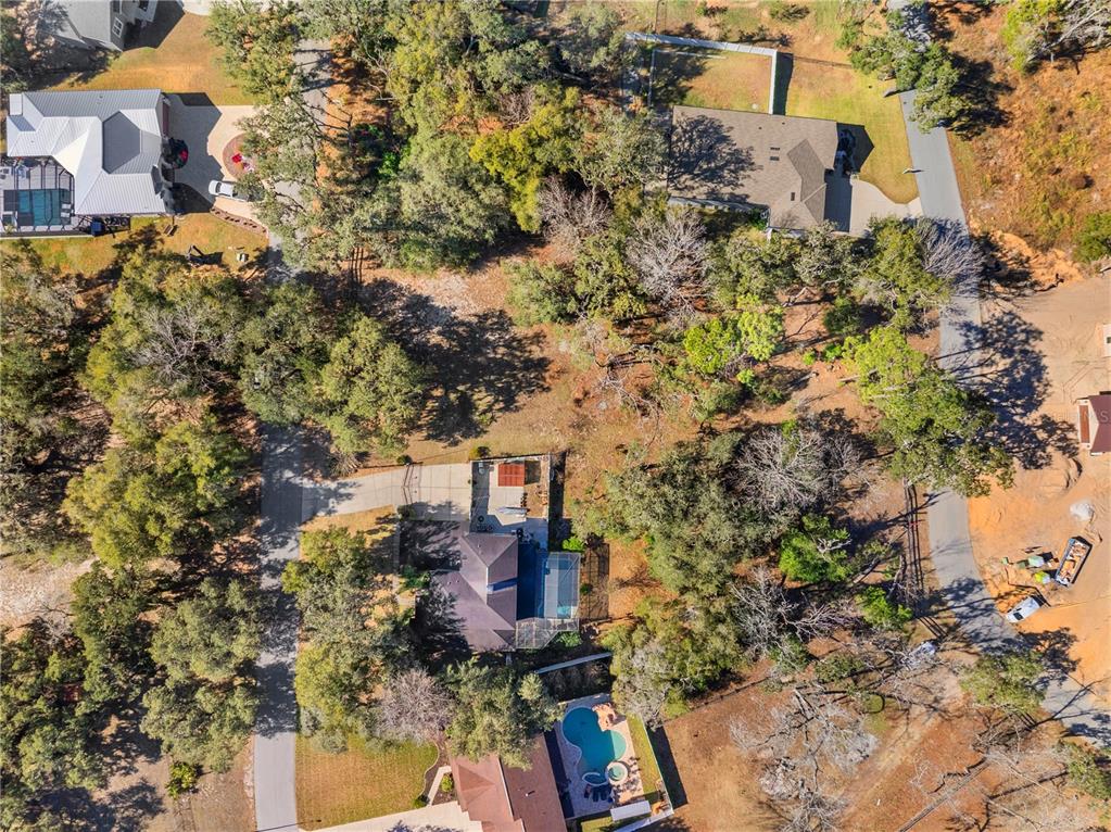 An aerial view shows several houses with swimming pools surrounded by trees and paved driveways — 5104 WESTLAKE BOULEVARD, DADE CITY, FL