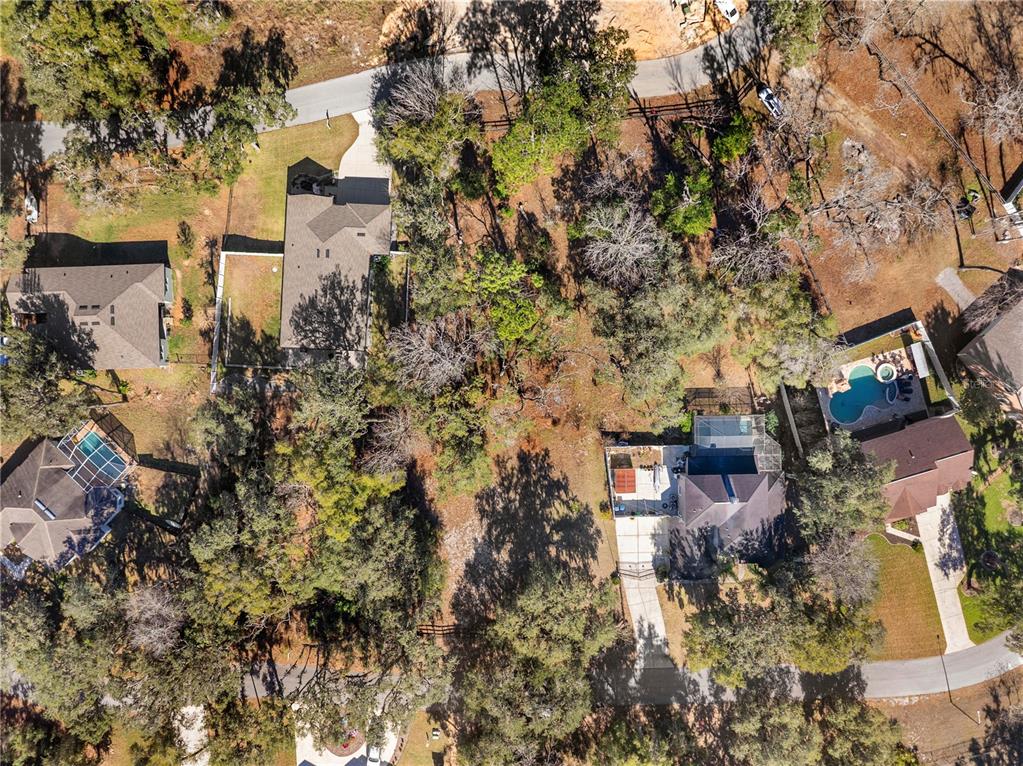 An aerial view shows several houses with swimming pools surrounded by trees and paved driveways — 5104 WESTLAKE BOULEVARD, DADE CITY, FL