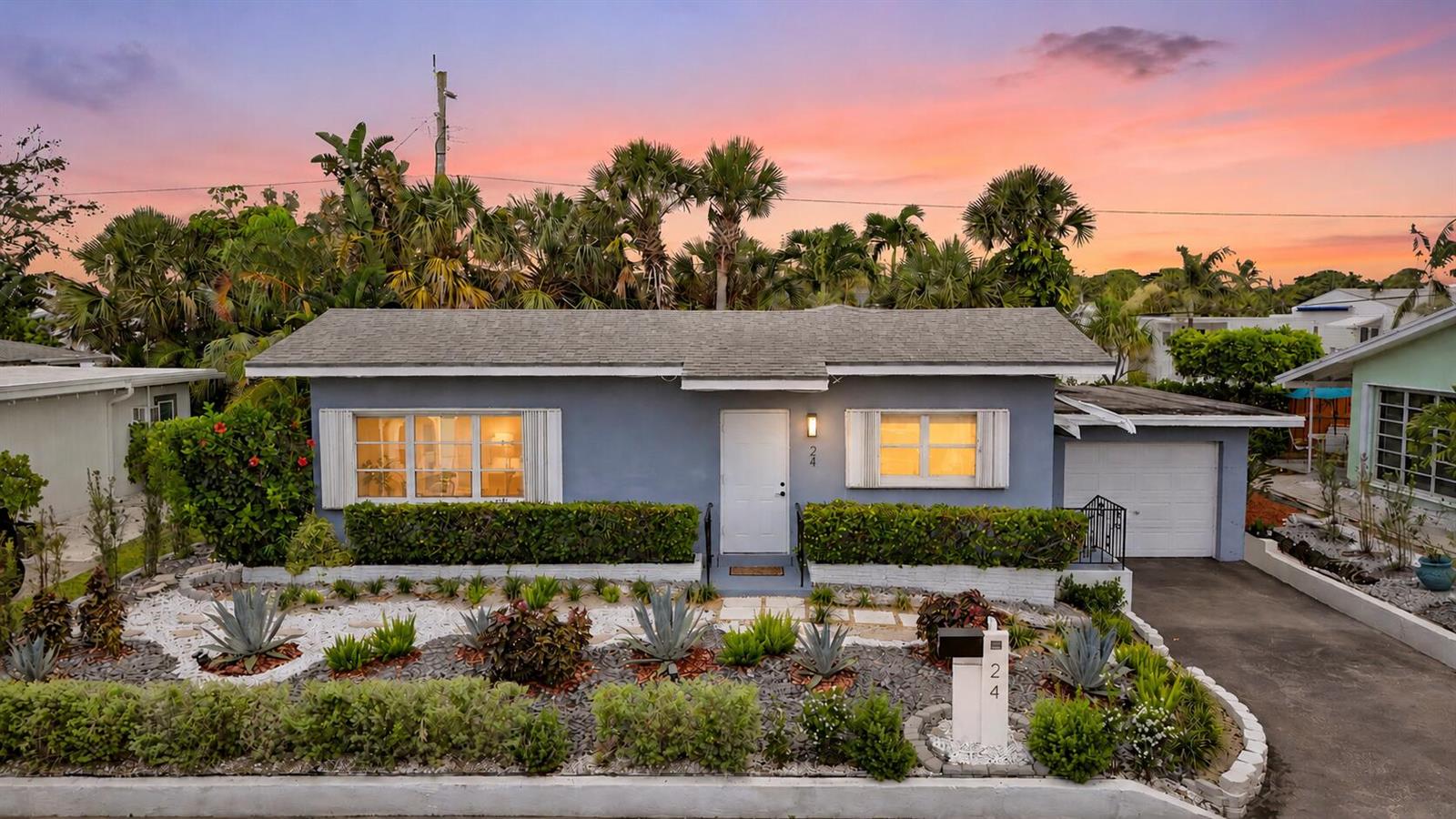 A blue single-story house with a white door, garage, and landscaped front yard at sunset — 24 Douglas Drive, Ocean Ridge FL 33435, OCEAN RIDGE, FL