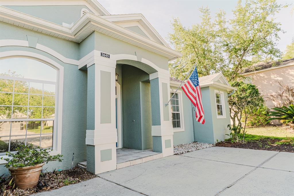 A light green house exterior features a covered entryway, white trim, and an American flag — 3645 ROCHELLE LANE, APOPKA, FL