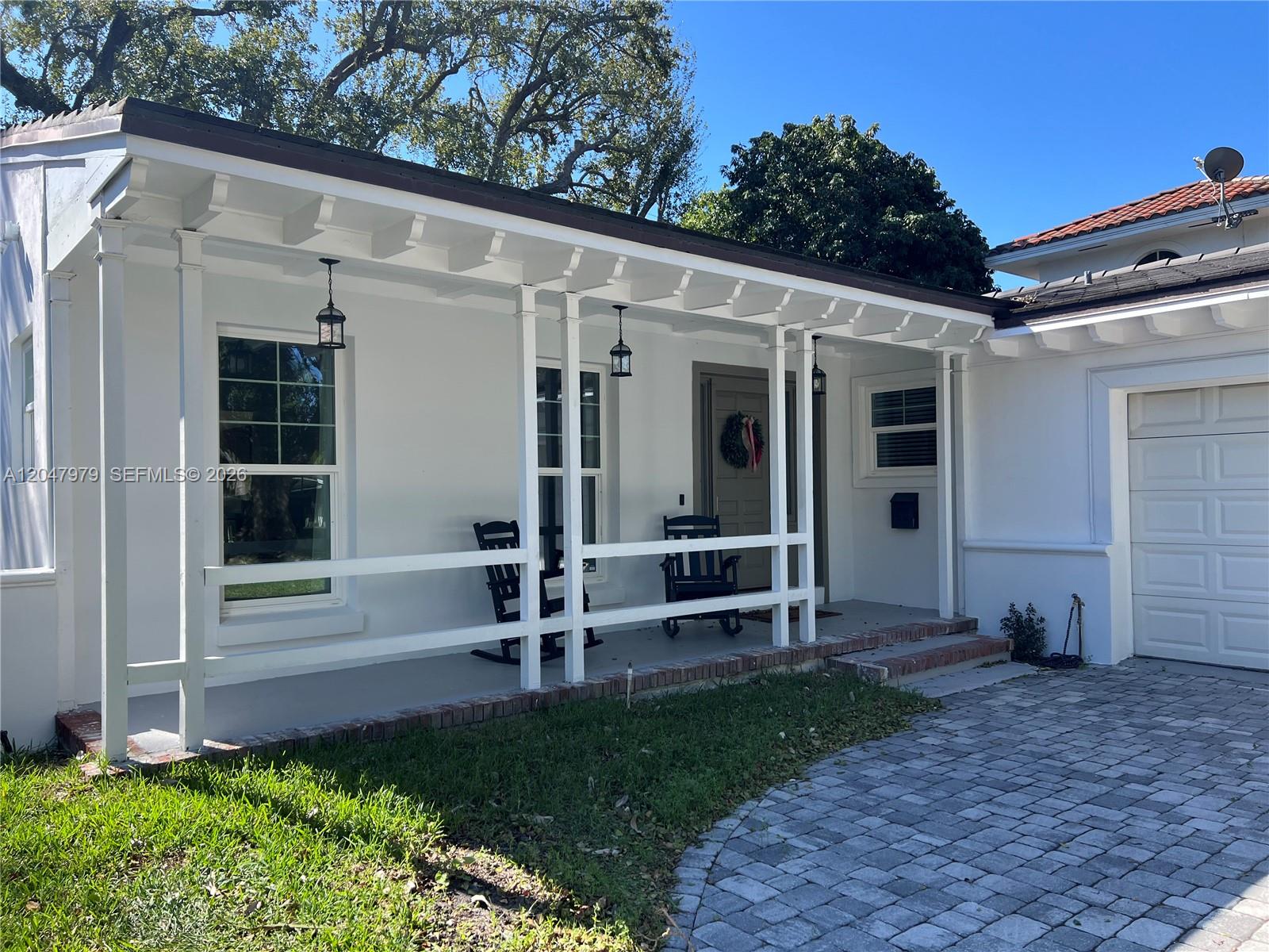 A white house exterior features a covered front porch with rocking chairs and brick steps — 1452 Urbino Ave, Coral Gables FL 33146, CORAL GABLES, FL