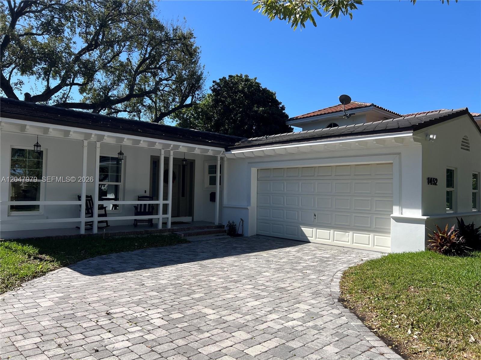 A white single-story house features a paved driveway, a covered front porch, and a garage — 1452 Urbino Ave, Coral Gables FL 33146, CORAL GABLES, FL