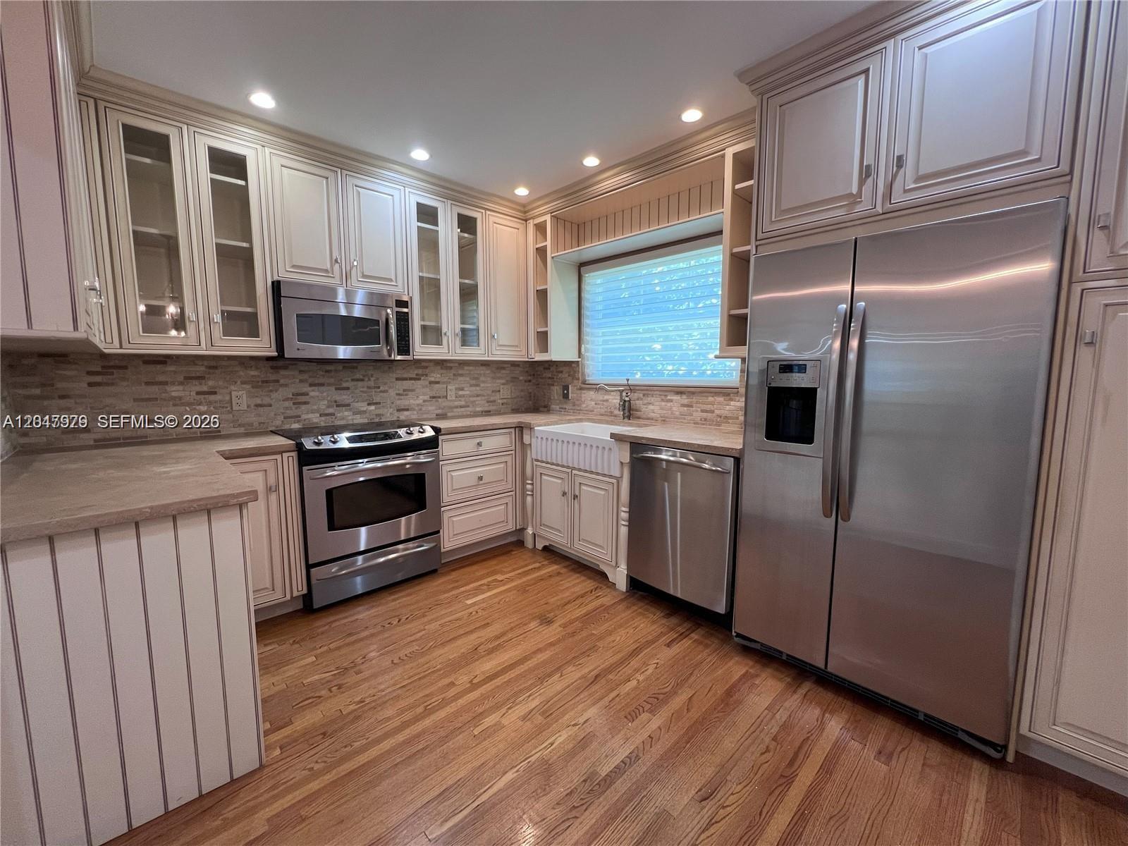 A kitchen features light-colored cabinetry, stainless steel appliances, a farmhouse sink, and hardwood flooring — 1452 Urbino Ave, Coral Gables FL 33146, CORAL GABLES, FL
