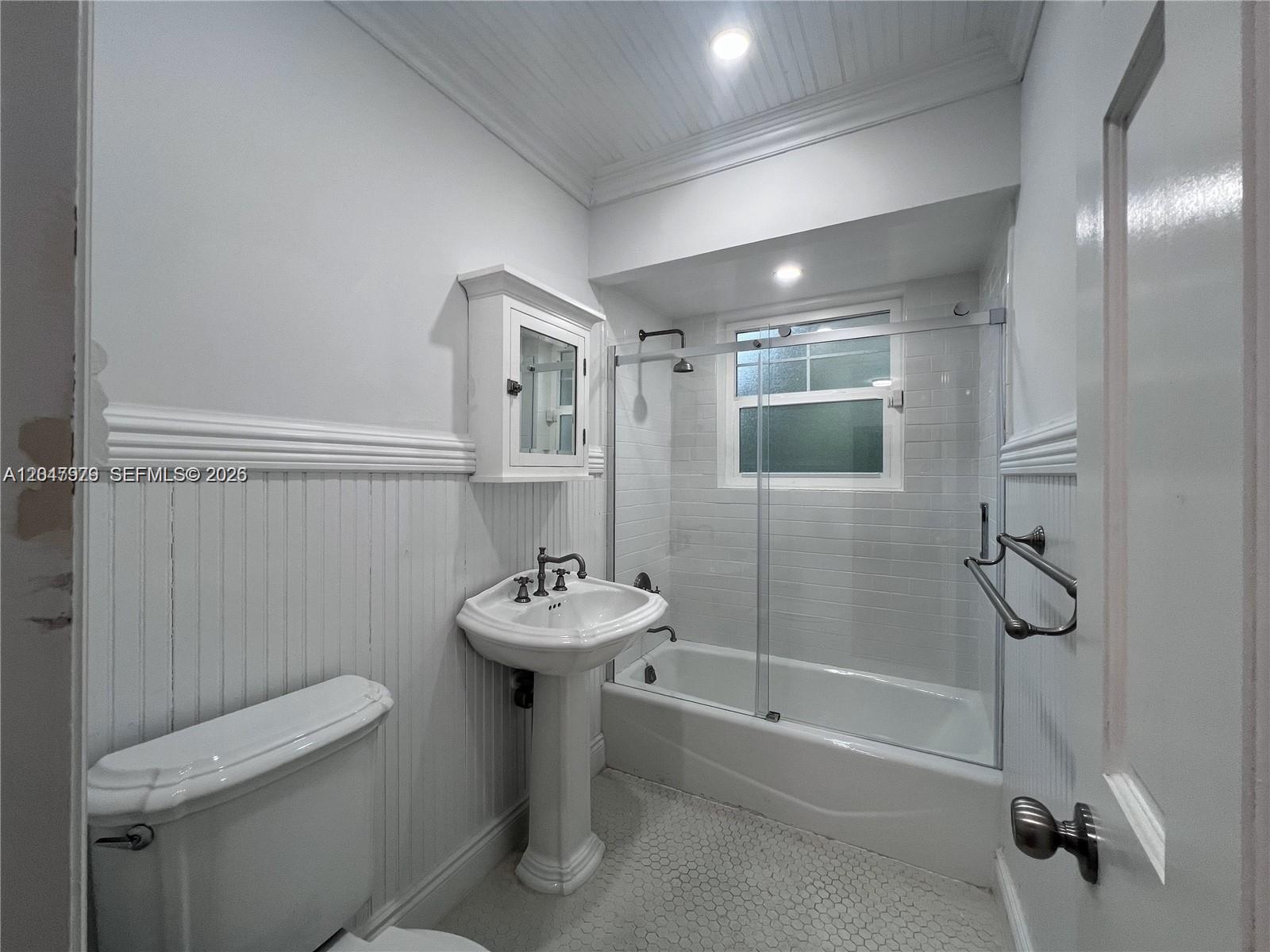 A bathroom features a pedestal sink, a toilet, and a bathtub with a glass shower door — 1452 Urbino Ave, Coral Gables FL 33146, CORAL GABLES, FL