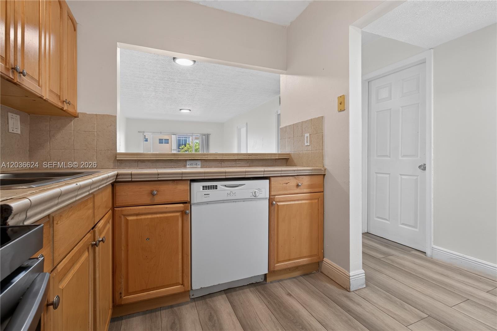 A kitchen features wood cabinets, tile countertops, a white dishwasher, and a pass-through window — 6070 W 18th Ave # 209, Hialeah FL 33012, HIALEAH, FL