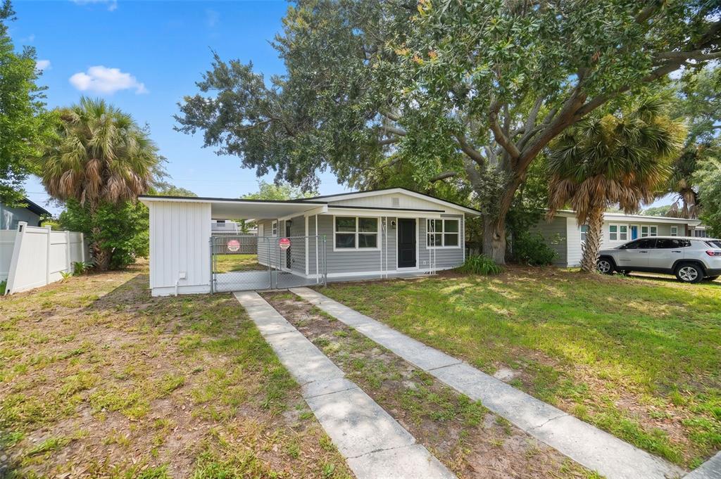 A single-story house with gray siding, a carport, and a concrete driveway under large trees — 4406 W WALLACE AVENUE, TAMPA, FL