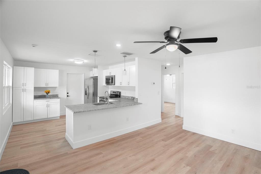 A kitchen with white cabinets, granite countertops, and light wood flooring opens to a living area — 4406 W WALLACE AVENUE, TAMPA, FL